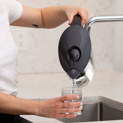 A woman pouring clean water from the Santevia MINA Alkaline Pitcher in black into glass#colour_black